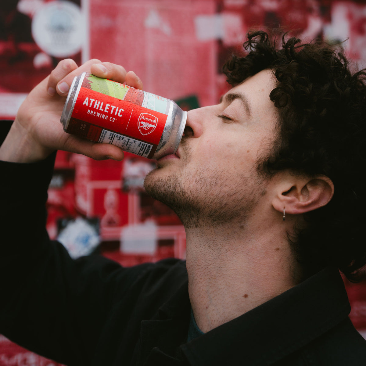 Person drinking from an Arsenal-branded Athletic Brewing can.